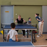Tennis de table - Yannick échange quelques balles avec un de nos jeunes membres devant Cindy en juge arbitre attentive pendant que Louis discute en arrière plan.
